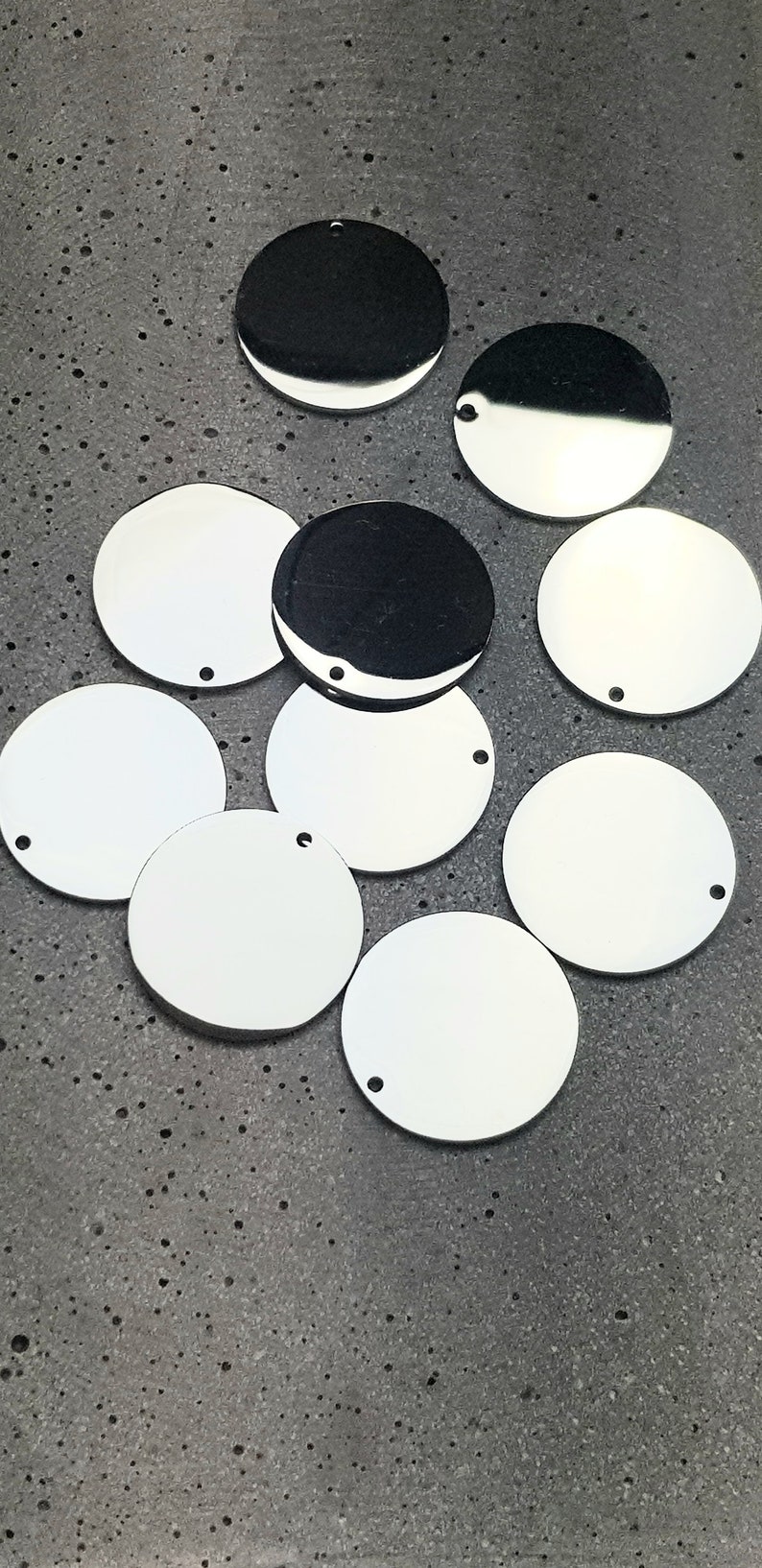 May include: A collection of nine silver-colored metal circles with a hole in the center. The circles are arranged in a random pattern on a gray textured surface.