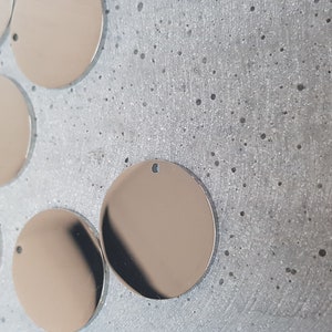 May include: A group of eight silver-colored metal circles with a hole in the center. The circles are arranged in a semi-circle on a gray textured surface.