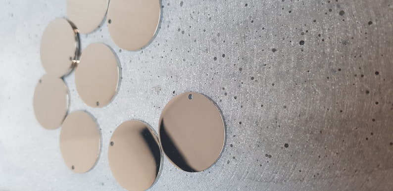 May include: A group of eight silver-colored metal circles with a hole in the center. The circles are arranged in a semi-circle on a gray textured surface.