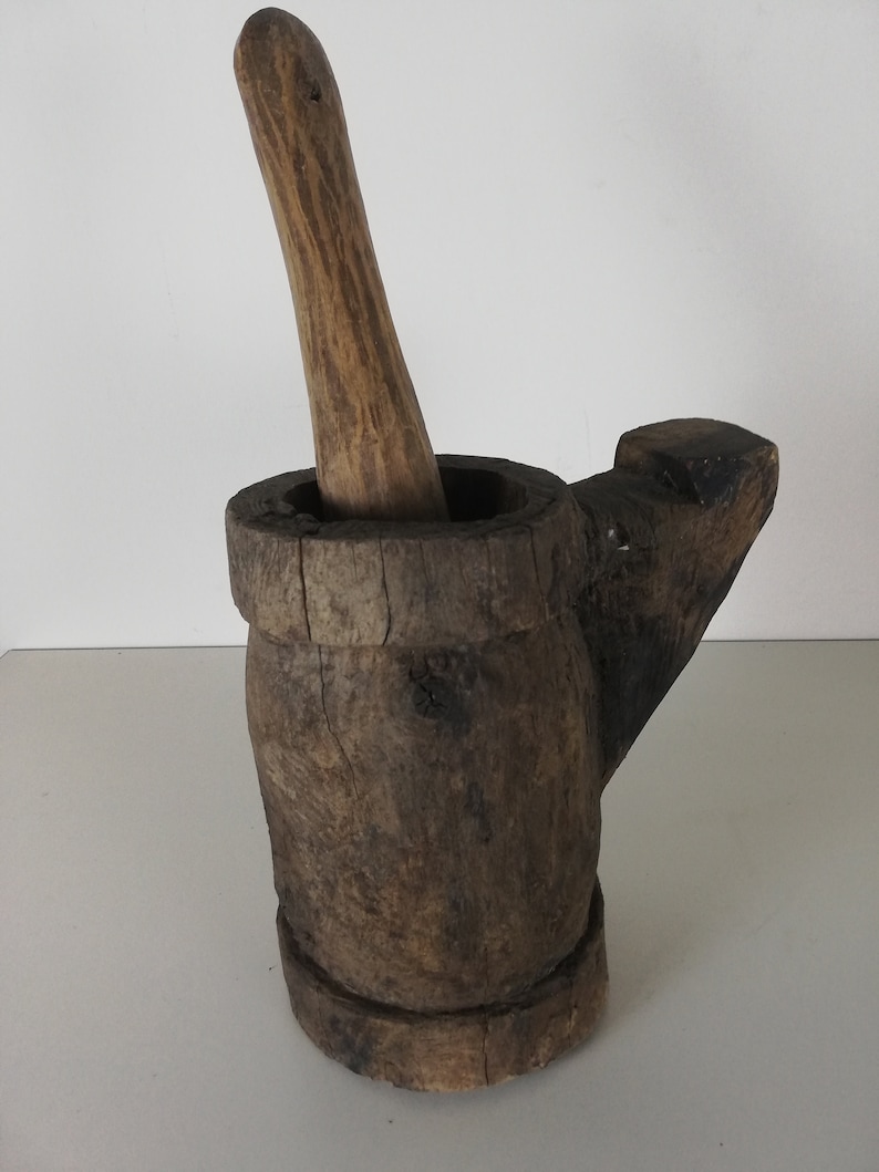 May include: A wooden mortar and pestle set. The mortar is brown and has a handle on the side. The pestle is also brown and has a rounded end.