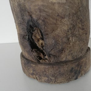 May include: A close-up of a wooden mortar and pestle with a worn, rustic appearance. The mortar has a large, round base and a smaller, round pestle. The wood is dark brown and has a rough texture.