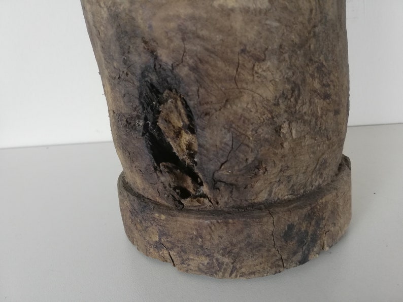 May include: A close-up of a wooden mortar and pestle with a worn, rustic appearance. The mortar has a large, round base and a smaller, round pestle. The wood is dark brown and has a rough texture.