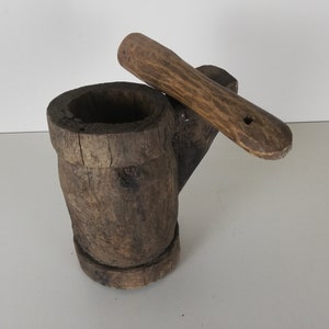 May include: A wooden mortar and pestle set. The mortar is made from a single piece of wood and has a natural, rustic finish. The pestle is also made of wood and has a smooth, rounded handle.