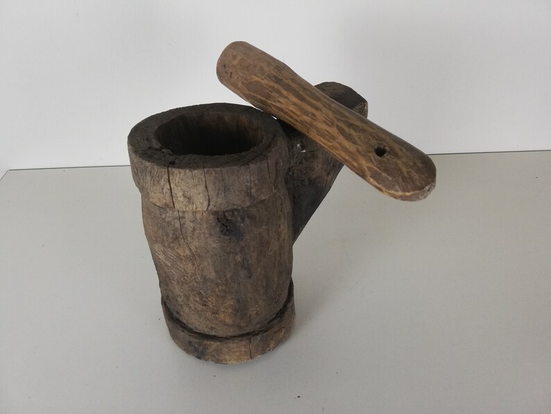 May include: A wooden mortar and pestle set. The mortar is made from a single piece of wood and has a natural, rustic finish. The pestle is also made of wood and has a smooth, rounded handle.