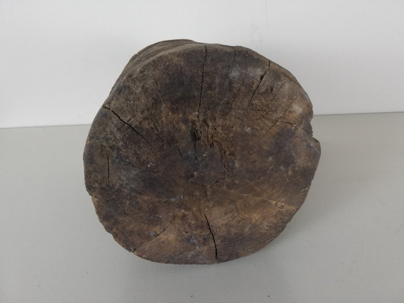 May include: A round, dark brown wooden stump with a rough, textured surface. The stump is a natural wood product and has a circular shape.