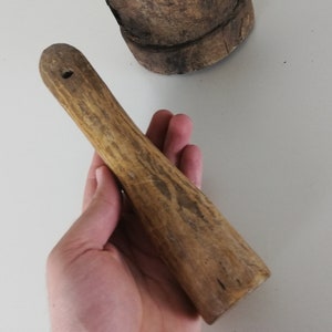 May include: A wooden pestle with a smooth, rounded top and a textured, slightly rough surface. The pestle is light brown in color and has a hole in the top.