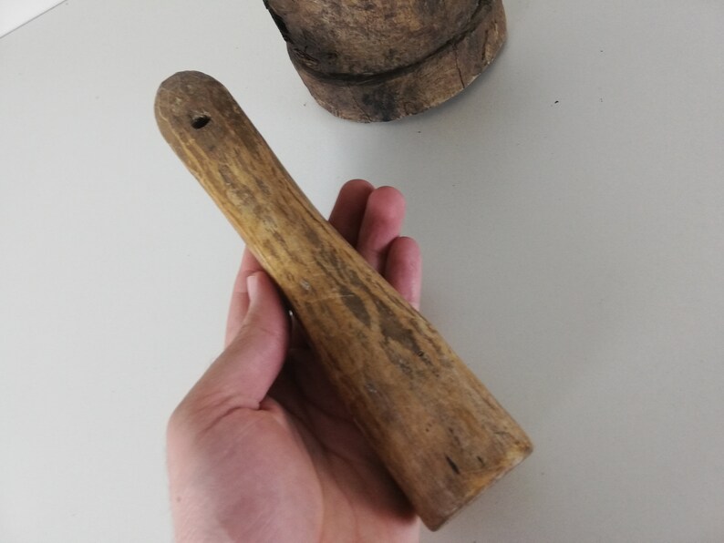 May include: A wooden pestle with a smooth, rounded top and a textured, slightly rough surface. The pestle is light brown in color and has a hole in the top.