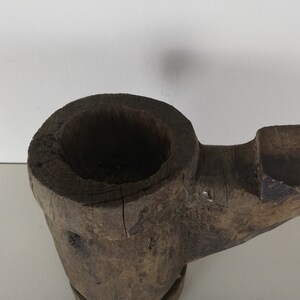 May include: A rustic wooden mortar and pestle with a dark brown finish. The mortar is shaped like a bowl with a wide opening and a rounded bottom. The pestle is a long, cylindrical piece of wood with a rounded end.