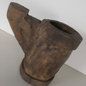 May include: A rustic wooden pipe with a wide, open bowl and a long, curved stem. The pipe is made of dark brown wood and has a rough, textured surface.