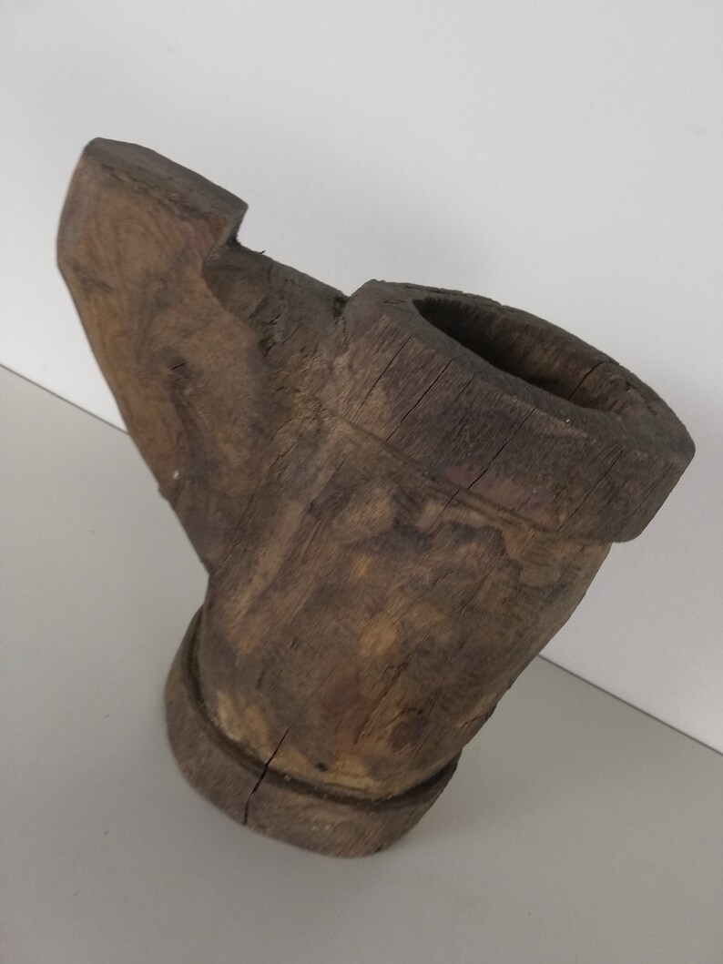 May include: A rustic wooden pipe with a wide, open bowl and a long, curved stem. The pipe is made of dark brown wood and has a rough, textured surface.