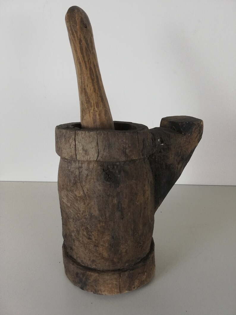 May include: A wooden mortar and pestle set. The mortar is brown and has a handle on the side. The pestle is also brown and has a rounded end.