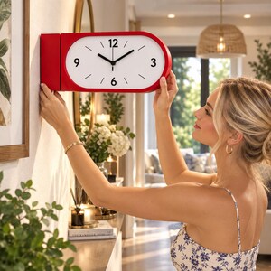 Può includere: Un orologio da parete orizzontale di forma ovale con una cornice rosso brillante e un quadrante bianco. L'orologio presenta numeri neri alle posizioni delle 3, 6, 9 e 12, con semplici tacche nere per le ore rimanenti e lancette nere.