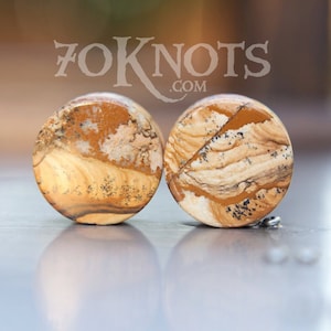 May include: Pair of brown and white stone ear gauges with a swirling pattern. 70Knots.com is printed on the background.