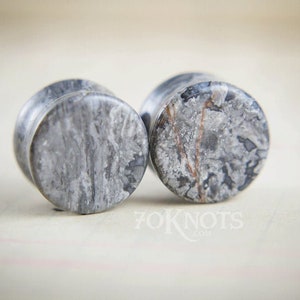 May include: A pair of gray and white marble stone ear gauges. The gauges have a swirling pattern of gray and white.