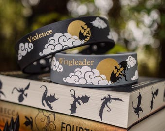 May include: Two leather bracelets featuring a black and gray color scheme with white cloud illustrations, a gold moon, and a black dragon silhouette. The black bracelet displays the word Violence, while the gray bracelet features the word Wingleader.