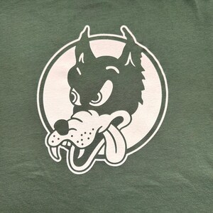 May include: A green t-shirt with a white circle graphic of a cartoon wolf with a snarling expression and a tongue sticking out.