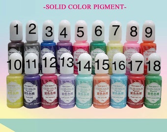 May include: Eighteen small bottles of solid color pigment, labeled with numbers 1 through 18. The bottles are arranged in two rows, with the first row containing bottles 1 through 9 and the second row containing bottles 10 through 18. Each bottle has a white cap and a clear glass body filled with a different color pigment. The bottles are labeled with the text "Solid Color Pigment" and the color name in Chinese characters.