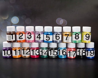 May include: Nineteen small glass bottles with white lids and labels with numbers 1 through 19. The bottles contain colorful glitter or mica powder.