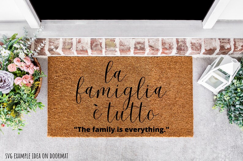 May include: A brown coir doormat with the text "la famiglia &egrave; tutto" in black cursive script. The text is translated below in English as "The family is everything."