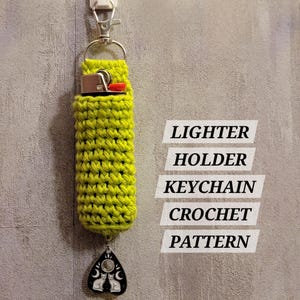 May include: A neon green crochet lighter holder keychain with a silver clasp. The holder has a black and silver charm with two cats, moons, and stars. Text on the image reads: Lighter Holder Keychain Crochet Pattern.