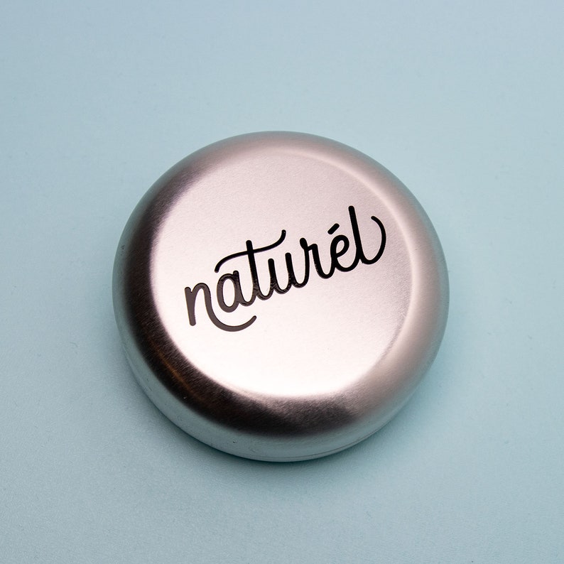 Op de afbeelding: Een ronde zilveren container met het woord "naturel" in zwarte cursieve letters.