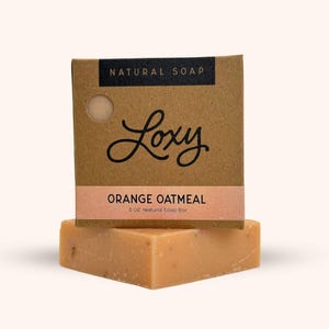 May include: A bar of orange oatmeal soap in a brown cardboard box with the text "NATURAL SOAP" and "Loxy" in black lettering. The box also says "ORANGE OATMEAL" and "5 OZ. Natural Soap Bar".