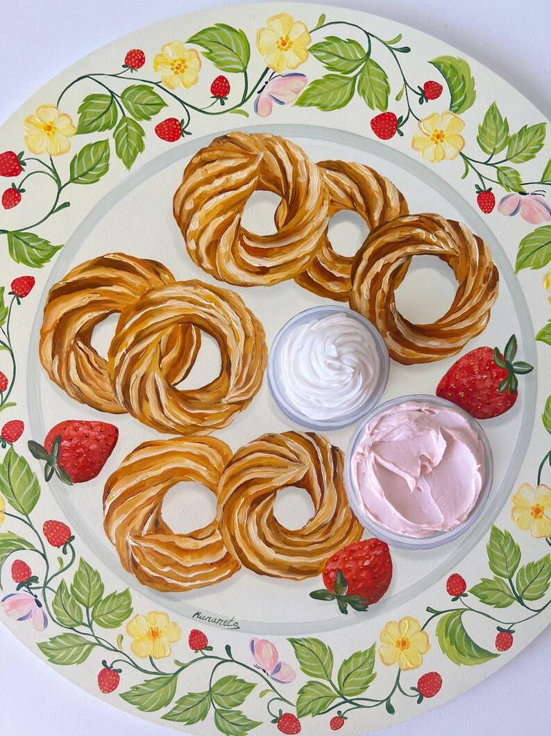 May include: A white plate with a decorative border of green leaves, yellow flowers, and red strawberries. The plate features five golden brown pastry rings, two small bowls of white and pink frosting, and four red strawberries.
