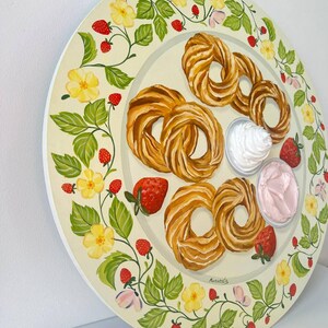 May include: A round, white plate with a green vine border featuring yellow flowers and red strawberries. The plate has a variety of pastries, including a few cream puffs, and two small bowls of whipped cream and pink frosting.