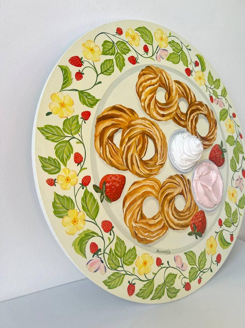 May include: A round, white plate with a green vine border featuring yellow flowers and red strawberries. The plate has a variety of pastries, including a few cream puffs, and two small bowls of whipped cream and pink frosting.