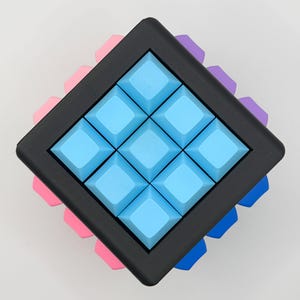 May include: A square puzzle with a black frame and nine light blue square buttons. The puzzle is surrounded by pink, purple, and blue accents. The puzzle is a brain teaser or a toy.