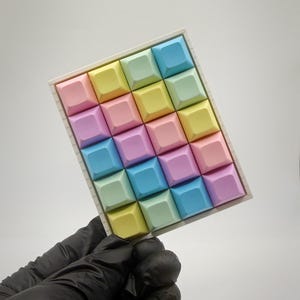 May include: A rectangular mechanical keyboard macro pad featuring a grid of twenty square keycaps in pastel shades of pink, yellow, blue, and green, set within a white frame. The keycaps are arranged in a four-by-five layout with a matte finish.