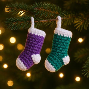 May include: Two miniature, handmade crochet Christmas stockings. One is purple, the other is green, both with white cuffs and heels. They hang from a pine branch, with soft, blurred lights in the background.
