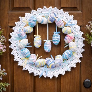 Könnte beinhalten: Ein handgefertigter Osterkranz mit einer weißen gehäkelten Deckchenbasis. Der Kranz ist mit bunten, gehäkelten Ostereiern in Pastelltönen von Blau, Gelb und Rosa geschmückt, die mit Bändern akzentuiert sind. Der Kranz wird an einer Holztür ausgestellt.
