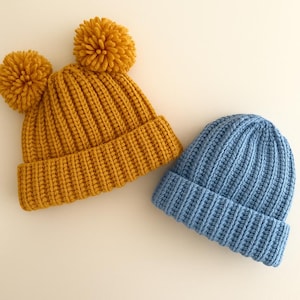 May include: Two knitted hats, one yellow with two pom-poms and one blue.