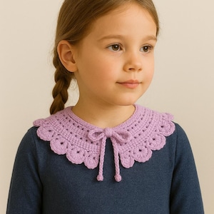 Könnte beinhalten: Ein lila gehäkelter Kragen mit einem gewellten Rand und einer zarten Schleife. Der Kragen wird über einem dunkelblauen Oberteil getragen. Die Häkelarbeit zeigt ein sich wiederholendes Muster aus kleinen Kreisen.