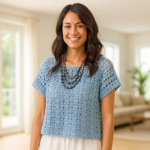 Könnte beinhalten: Hellblaues Häkeltop mit kurzen Ärmeln und rundem Ausschnitt. Das Oberteil hat ein offenes, luftiges Design. Eine mehrsträngige Perlenkette wird dazu getragen. Die Person trägt eine weiße Hose.