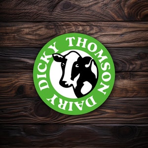 May include: A round green sticker with the text "DICKY THOMSON DAIRY" in white. The sticker features a black and white cow illustration in the center. The sticker is set against a dark wood grain background.