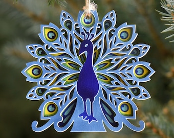 May include: A flat, laser-cut wooden ornament shaped like a peacock with its tail feathers fanned out. The design features shades of blue, green, and yellow, with intricate cutouts forming the eye patterns of the feathers and a jute twine loop.