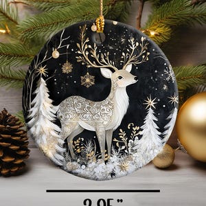 May include: A round Christmas ornament featuring a deer design. The deer has gold antlers and decorative patterns on its body, set against a black background with white trees and snowflakes. The ornament is 2.95 inches in diameter.