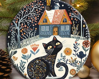 May include: A black cat with gold accents sits in a snowy landscape with a small house in the background. The ornament is decorated with a whimsical, folk art style.