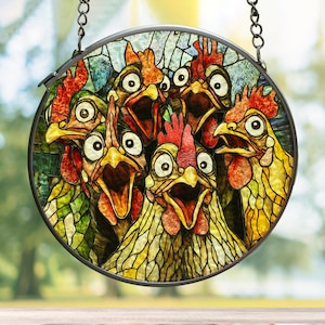 May include: A circular stained glass suncatcher featuring a group of five chickens with wide eyes and open beaks. The chickens are rendered in shades of yellow, orange, and red with green accents, all enclosed within a dark metal frame and hanging chain.
