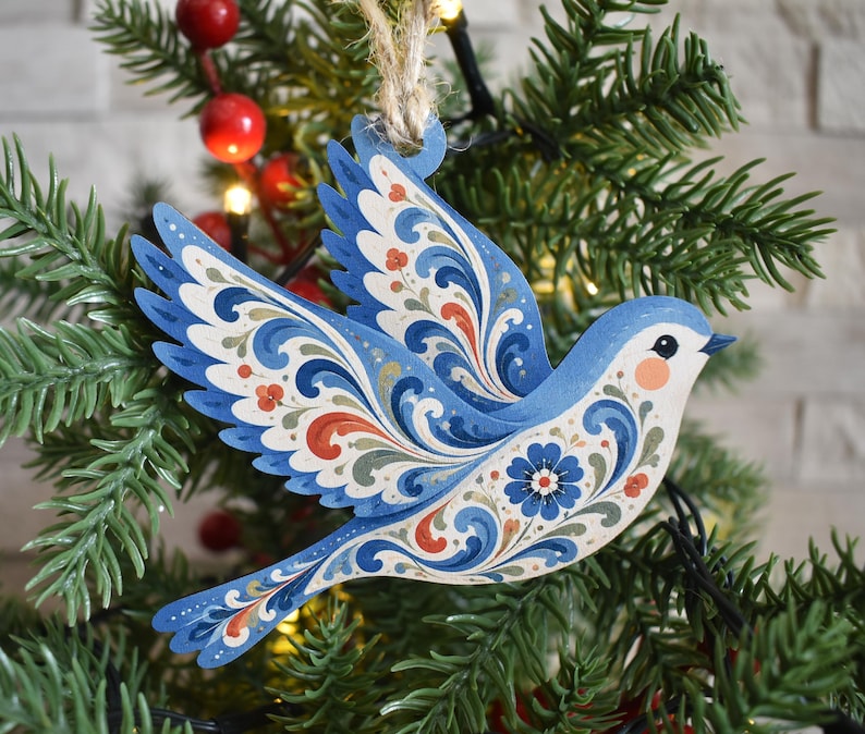 K&ouml;nnte beinhalten: Ein flacher, vogelf&ouml;rmiger Holzanh&auml;nger mit komplexen floralen Rankenmustern in Blau, Wei&szlig; und Orange. Der Vogel ist im Flug mit nach oben ausgebreiteten Fl&uuml;geln dargestellt und an einer Schlaufe aus nat&uuml;rlichem Jutegarn befestigt.