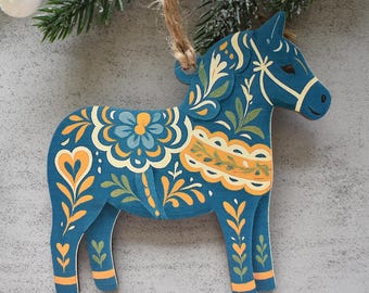 May include: A flat, blue wooden horse ornament featuring intricate yellow and light blue floral patterns, heart motifs, and decorative scrollwork. The horse is suspended by a natural jute twine loop and includes a small white pom-pom detail.
