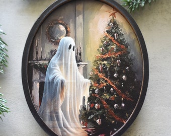 May include: An oval-shaped wooden Christmas ornament featuring a printed illustration of a white sheet ghost standing beside a decorated pine tree. The scene includes a fireplace, a mirror, and a star topper, all framed in a dark brown wood border.