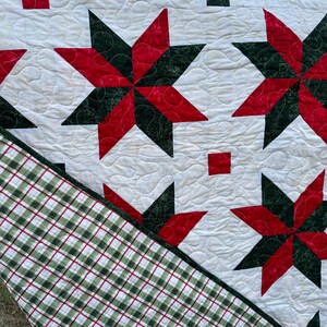 May include: A white quilt with a green and red star pattern. The quilt is quilted with a swirl design. The quilt has a green and white plaid backing.