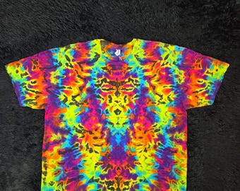 Może przedstawiać: Koszulka z krótkim rękawem z żywym, symetrycznym wzorem tie-dye w kolorach neonowej żółci, jasnego pomarańczu, elektrycznego błękitu i głębokiego fioletu. Wzór przedstawia skomplikowane, wirujące organiczne kształty na całej tkaninie.