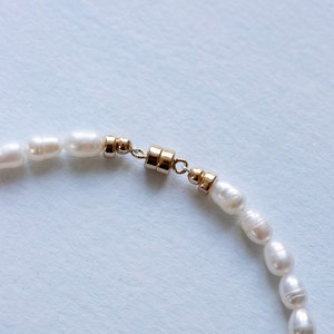 Closeup view of luxury freshwater pearl anklet gold closure on blue backdrop