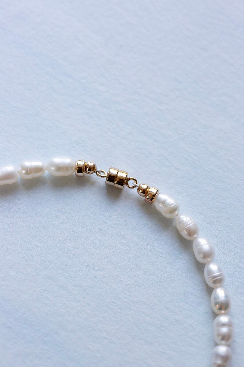 Closeup view of luxury freshwater pearl anklet gold closure on blue backdrop