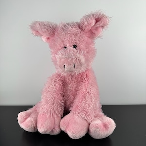 May include: A pink plush pig toy with large ears, a snout, and four legs. The pig is sitting upright, with its front legs extended. The fur is soft and fluffy, and the pig has black eyes.