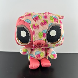 Puede incluir: Juguete de peluche rosa con un patrón de espiral colorido y grandes ojos negros. El juguete tiene una pequeña nariz rosa y una sonrisa cosida.